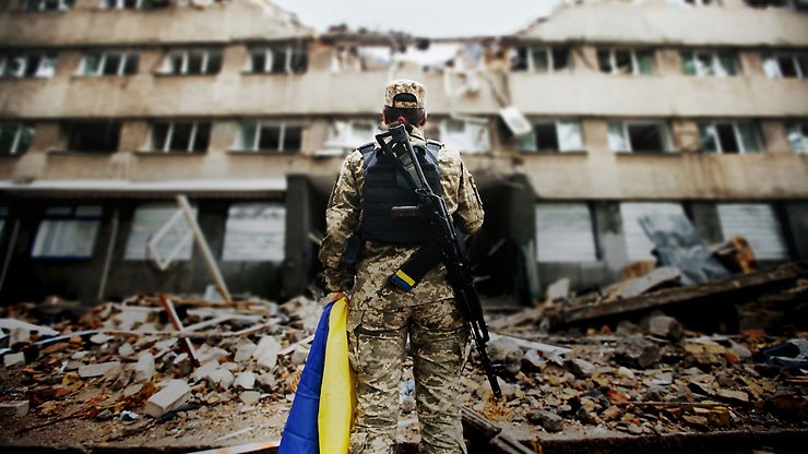 Soldat står med Ukrainas flagga i ett krigshärjat område.