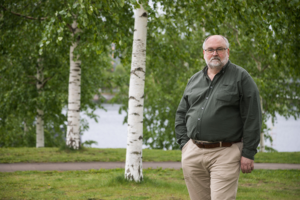 Håkan Andersson i rutig skjorta framför en husvägg