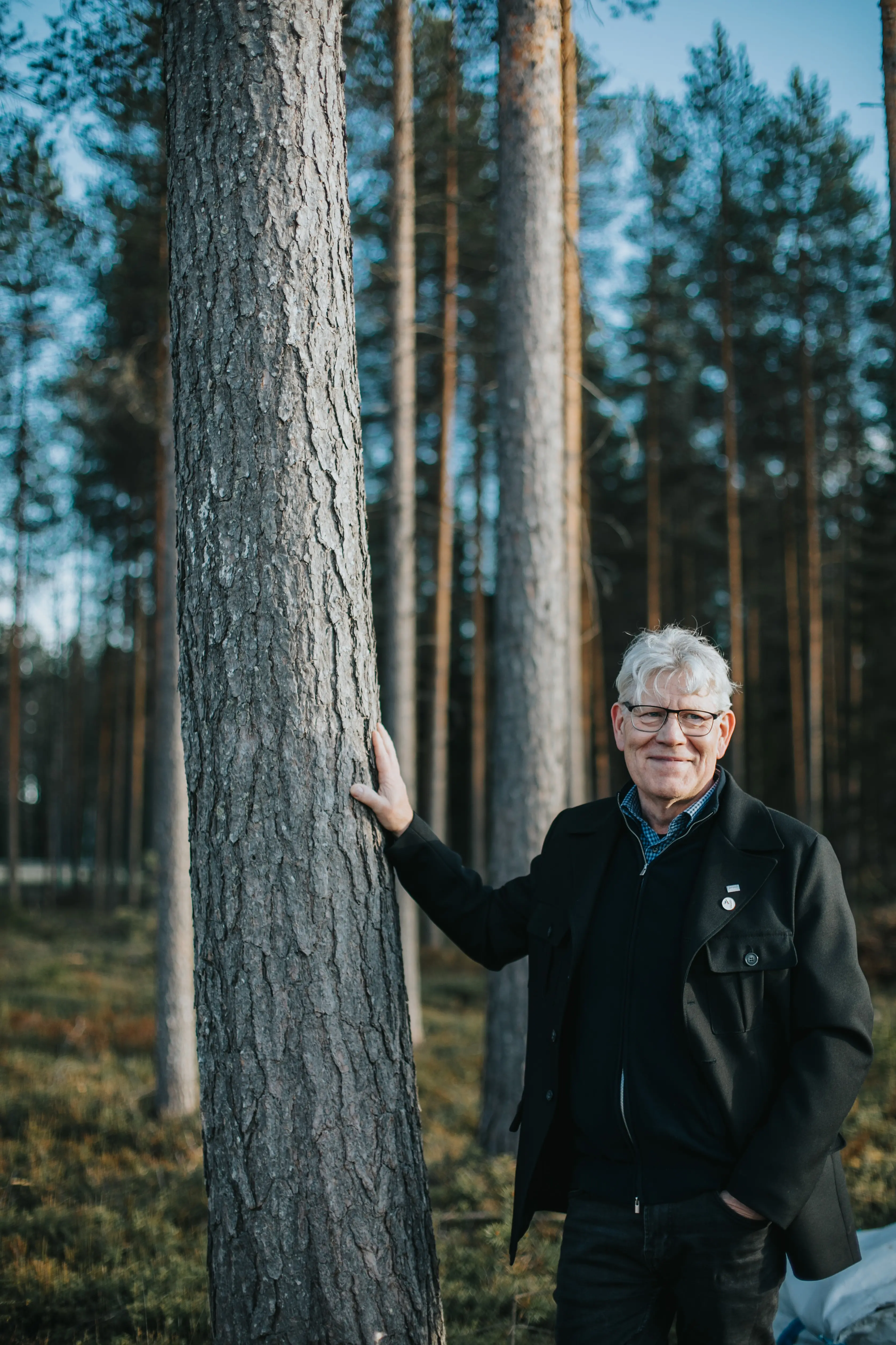 Anders Nilsson står stabilt med högerhanden mot en reslig tall och klädd i svart.
