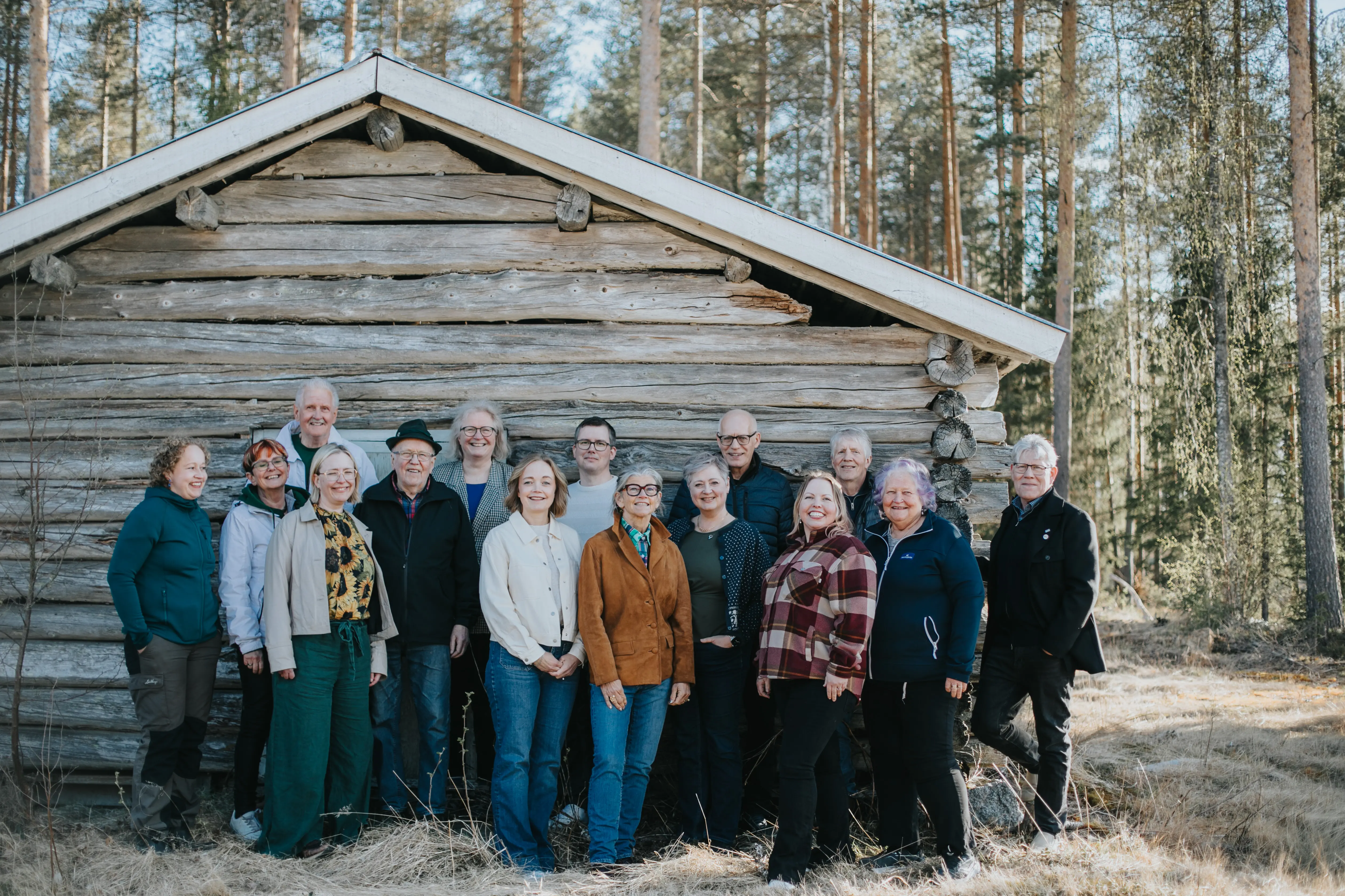 Huvuddelen av de som kandiderar för Centerpartiet Vännäs i valet till kommunfullmäktige 2026 står i grupp uppställda mot gaveln av en lada med grånat timmer.