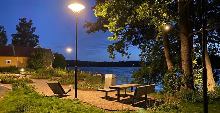 Upplyst plats med bänkar och bord i Skönviksparken vid sjön Flaten i rönninge.