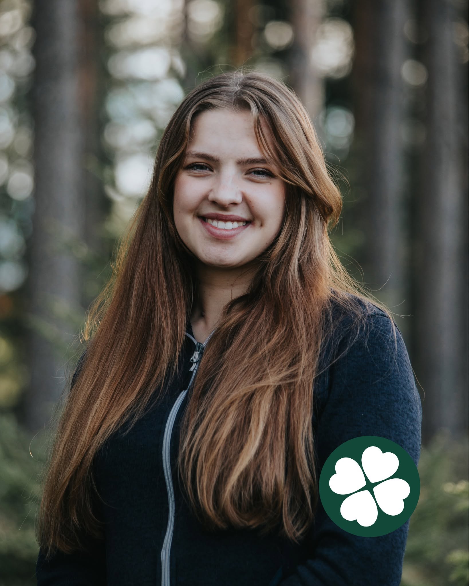 Emmy Lundberg leende i profil med tallar i bakgrunden och Centerklövern nere till höger i bild.