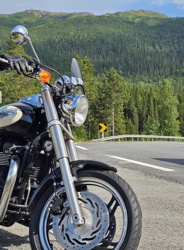 MC Triumph sticker in med fronten från höger och man en att den står i ytterkurva ovan en slingrig backe.