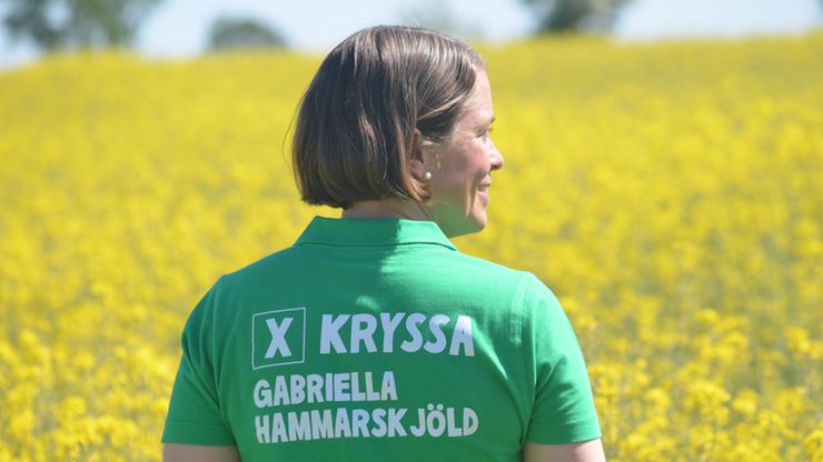 Gabriella tittar ut över rapsfält iklädd grön piké med texten "Kryssa Gabriella" på