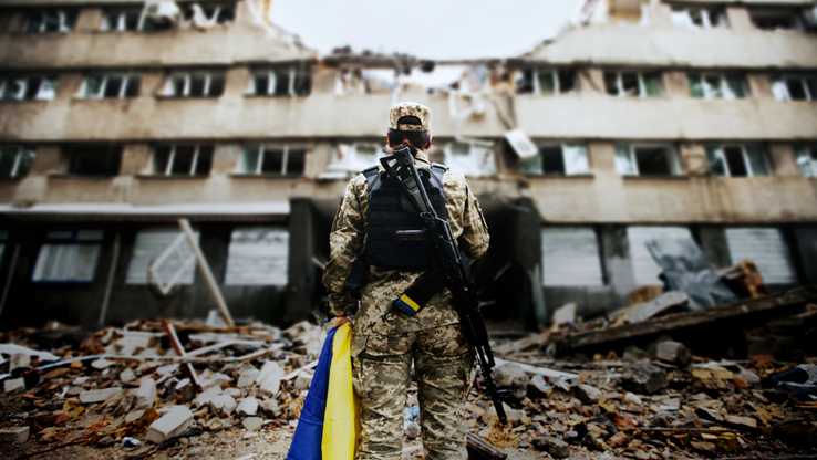 Bild på soldat framför sönderbombat hus i Ukraina