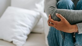 Kvinna sitter vid en säng och tar sig runt kroppen