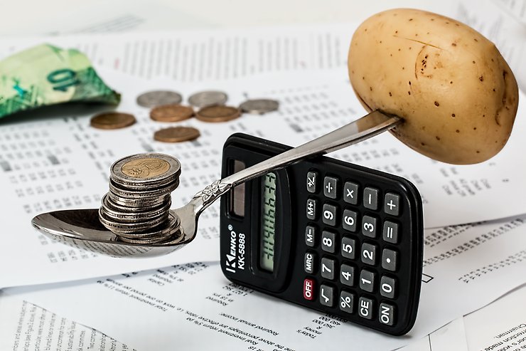 en sked balanserar en potatis och mynt på en miniräknare som står på högkant