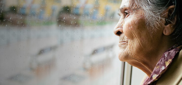 Äldre kvinna som tittar ut genom ett fönster